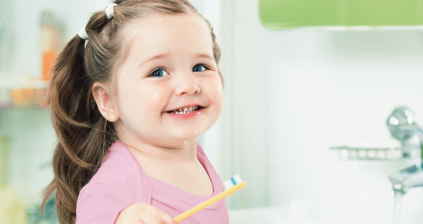 a girl toddler smiling and holding a tooth brush