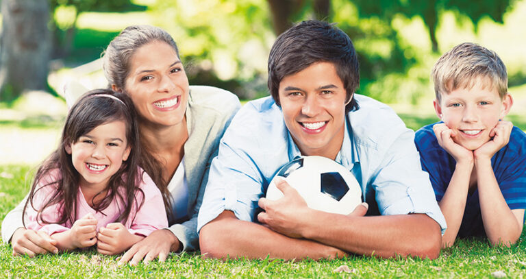 Family lies on the grass and smiles to reveal post-Invisalign teeth