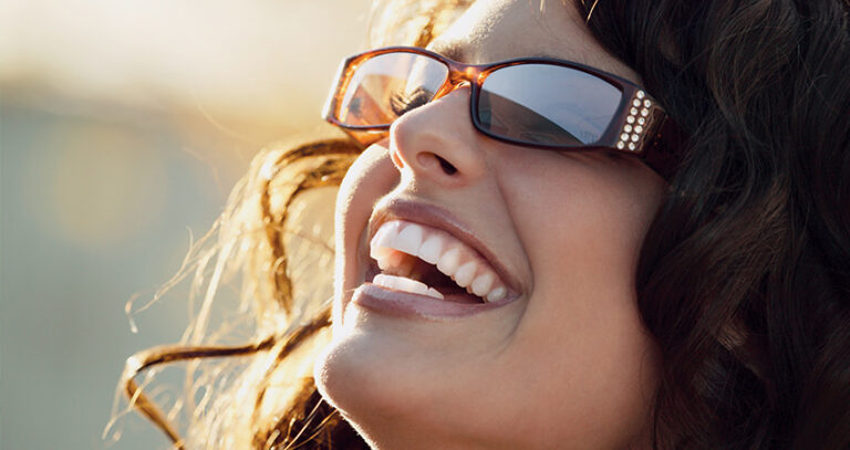 caucasian woman in sunshine smiling head tilted back sunglasses