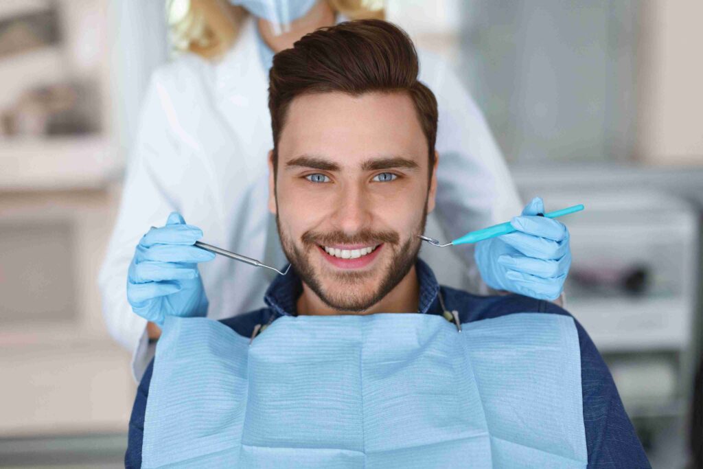 Smiling patient during a dental exam with dentist tools ready.
